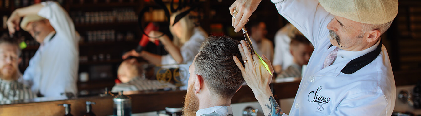 Barber fra Sam's Barber klipper, barberer og styler hår på kunde.